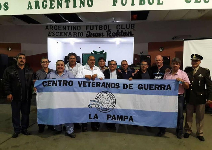 En la fotografía se muestra a ex – combatientes de la Guerra de Malvinas con una bandera argentina con la leyenda: “Centros de Veteranos de la Guerra La Pampa”.