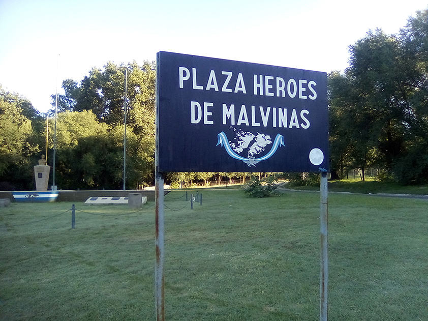 La fotografía muestra un cartel indicando que es la Plaza “Héroes de Malvinas”, en Cosquín, Prov. de Córdoba.