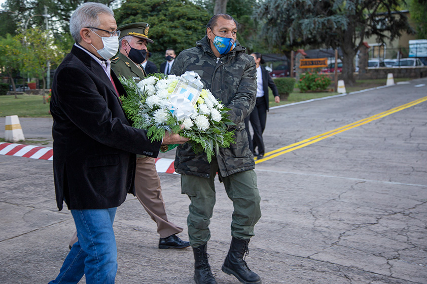 La fotografía muestra a Veteranos de la Guerra de Malvinas llevando una ofrenda floral al monumento en homenaje a los caídos de la Guerra de Malvinas. Más alejado se puede visibilizar al Teniente Coronel